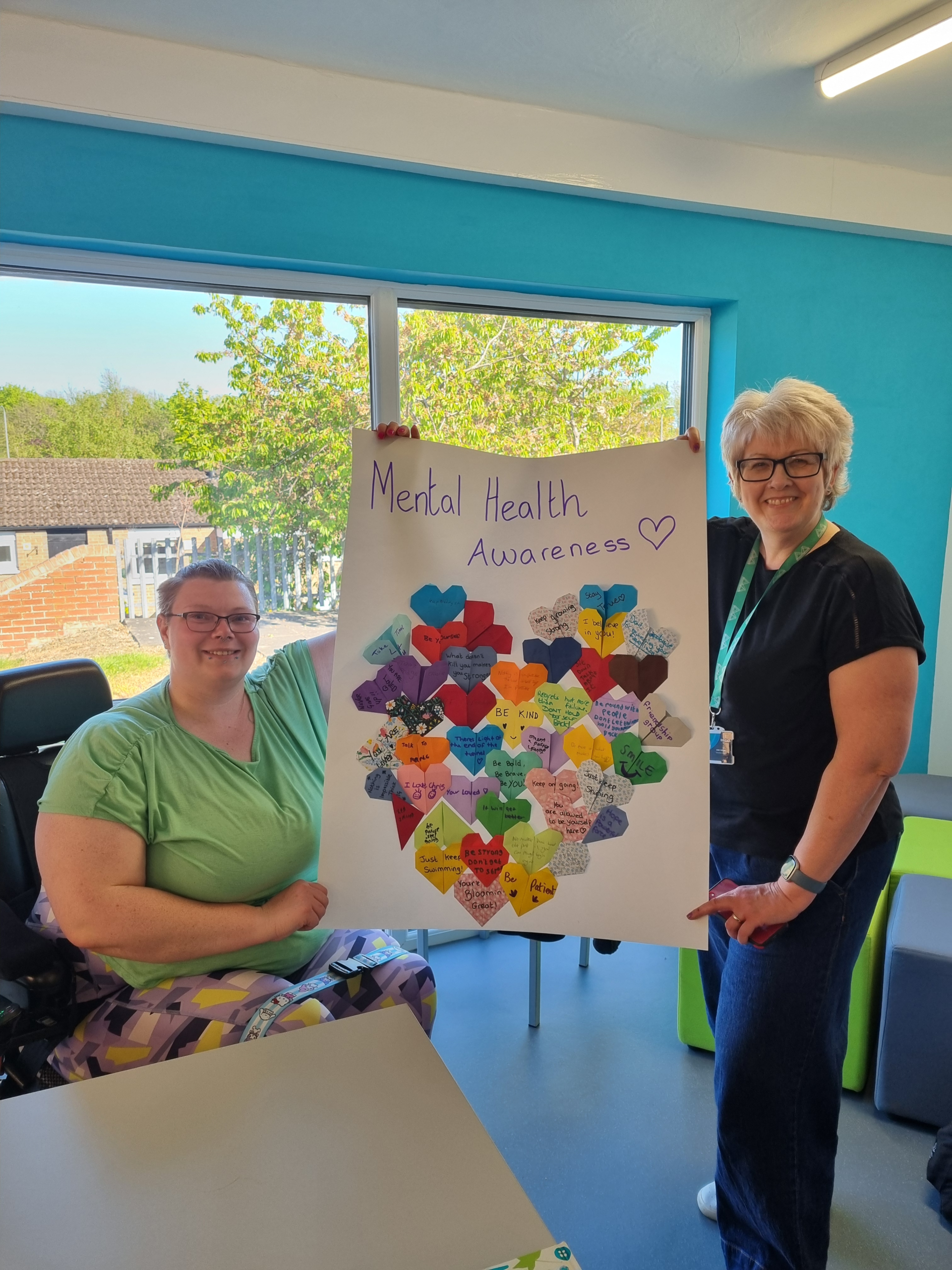 A person in a wheelchair and a person standing holding a piece of artwork between them.