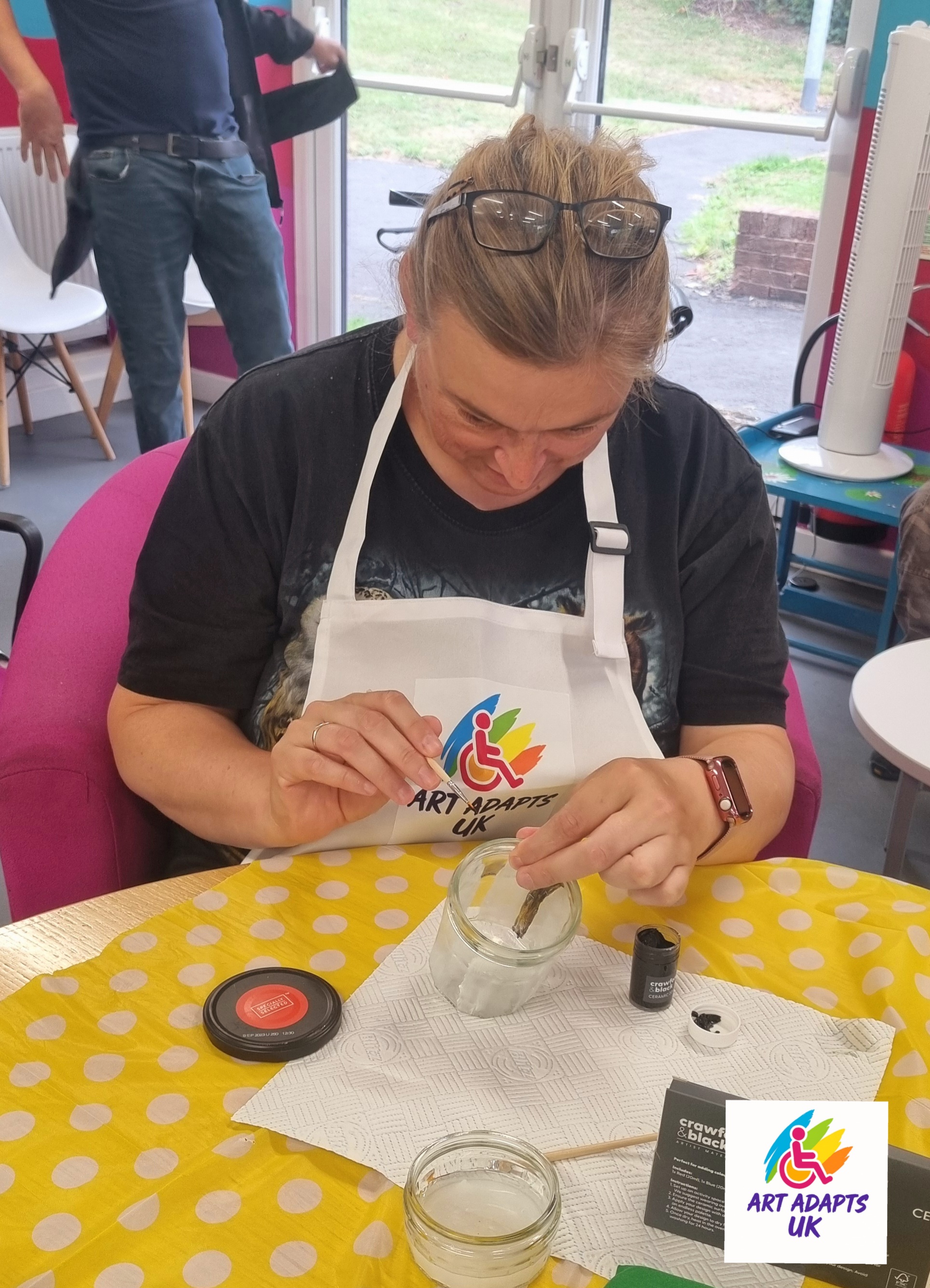 Lady in a white apron painting a glass jar at a table