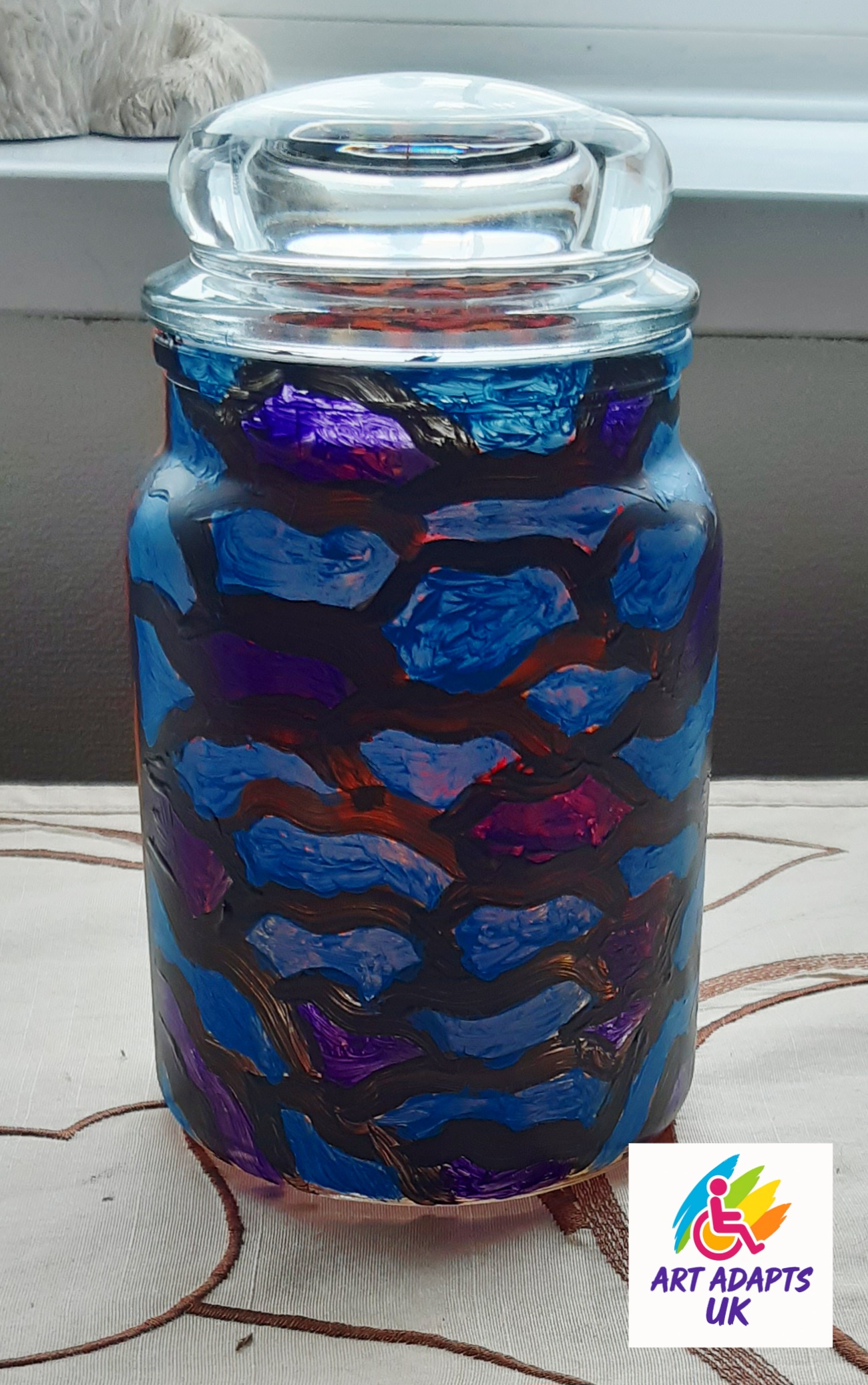 One side of a large jar painted to look like waves. Black outlines of the curves with various shades of blue filling in the segments. The opposite side of the jar is a different design in red