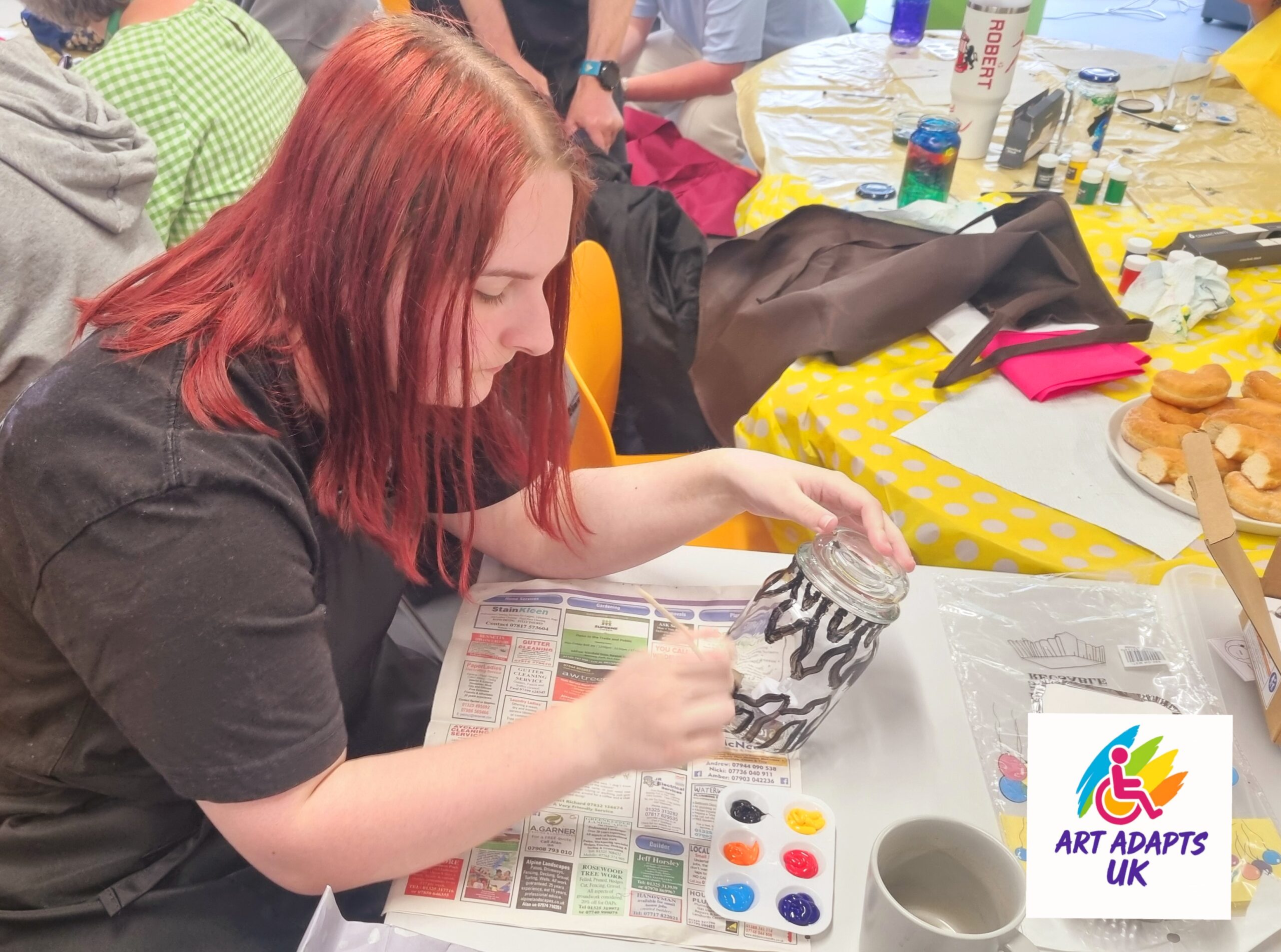 Young Lady sat at a table painting a large glass jar with black wavy lines