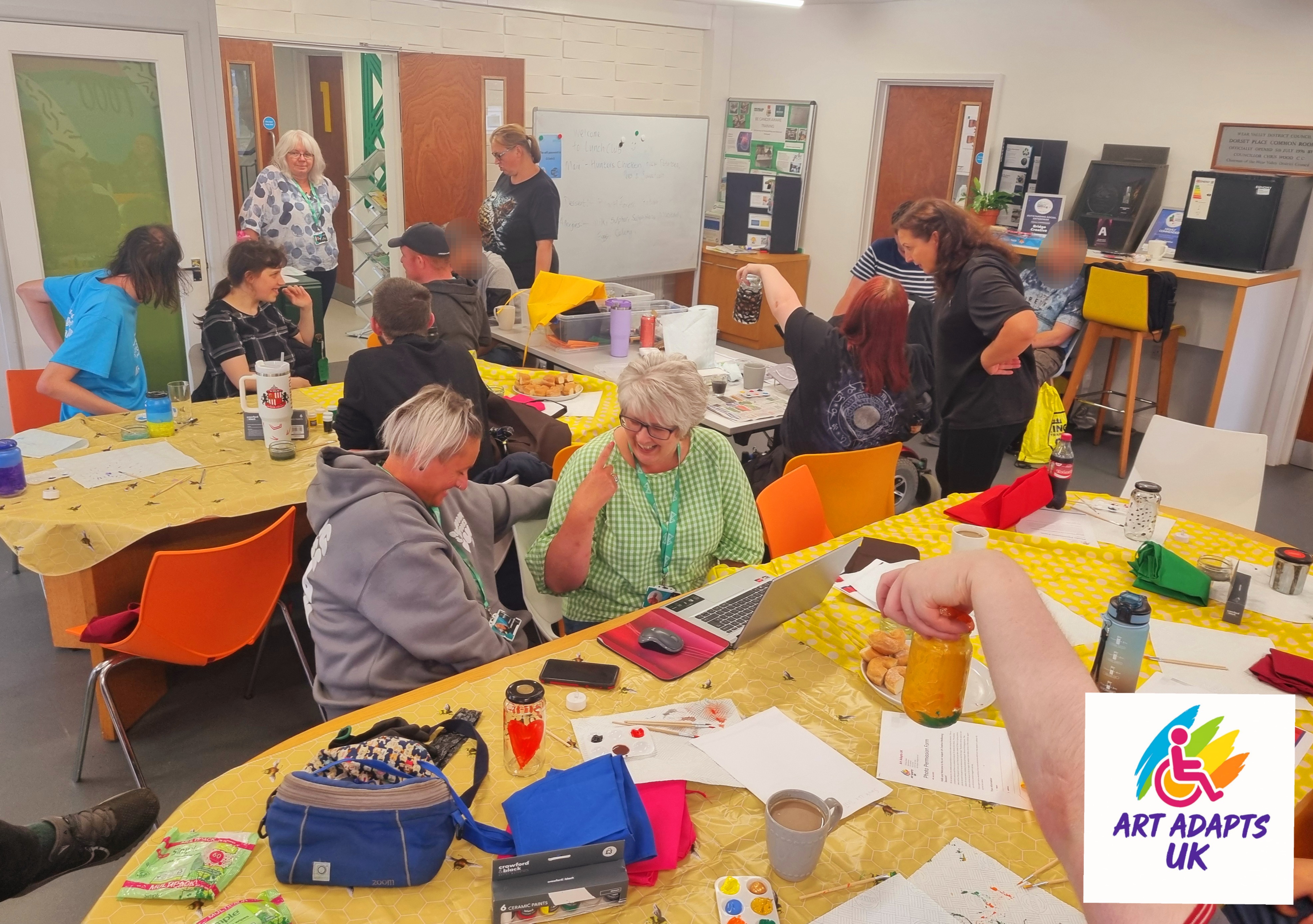 Group of people glass painting at 2 tables, with 2 ladies talking in the middle