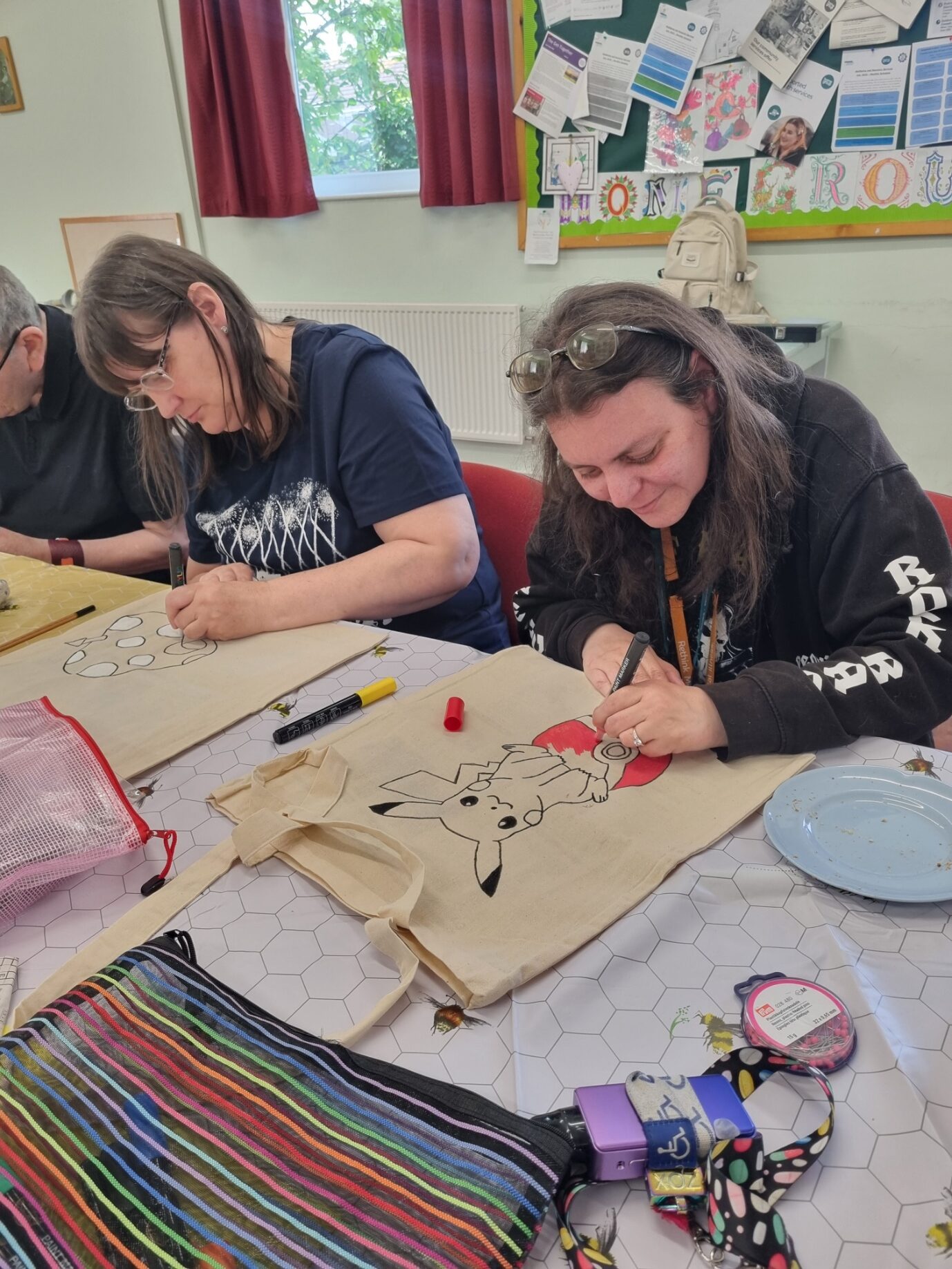 2 women talking while taking part in a canvas bag painting activity using paint pens